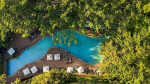 Vue aérienne d’un complexe hôtelier doté d’une piscine, entourée d’une végétation luxuriante et agrémentée d’espaces de détente.