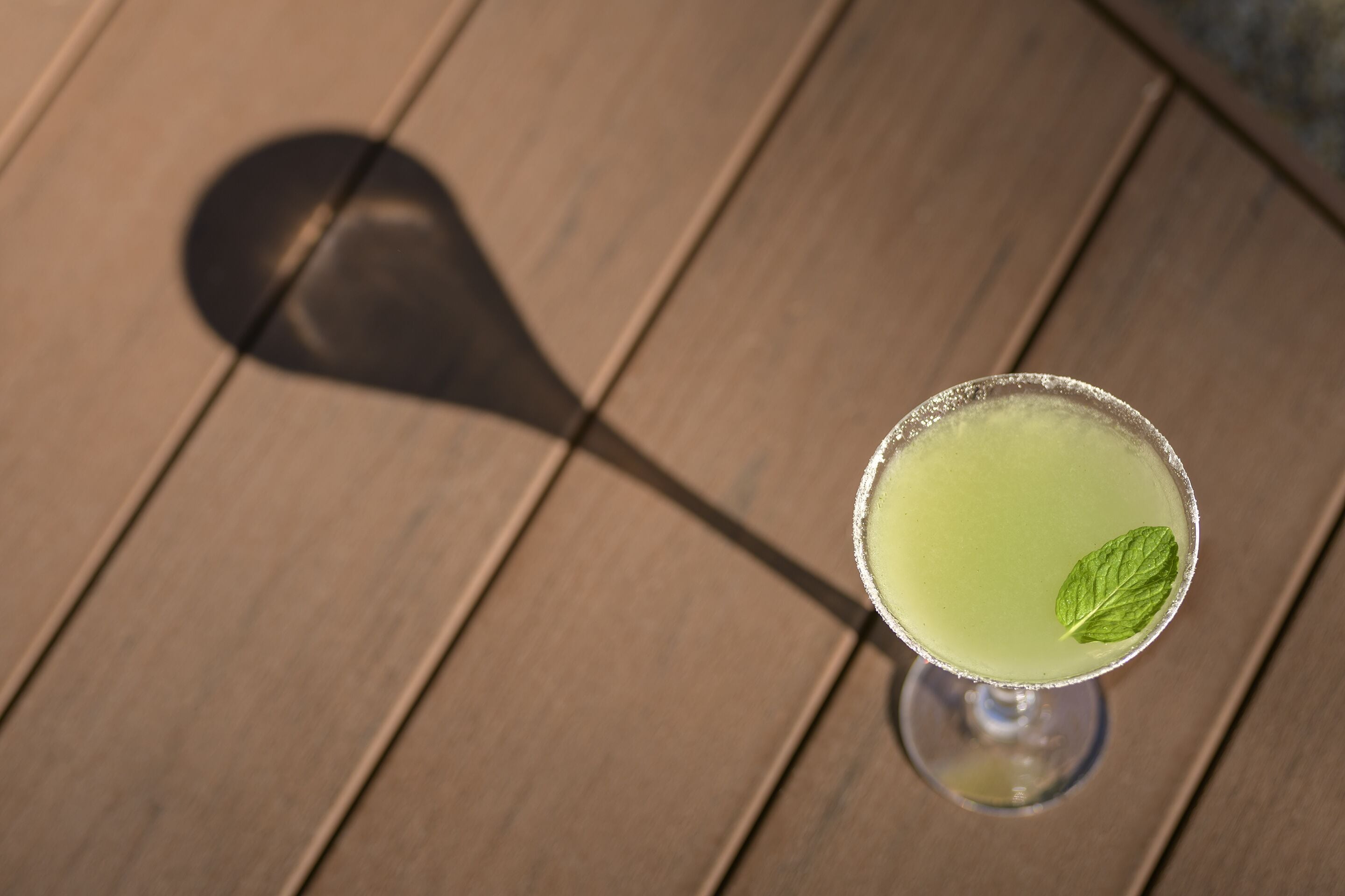 Un verre à cocktail orné d’une feuille de menthe, posé sur une table en bois.