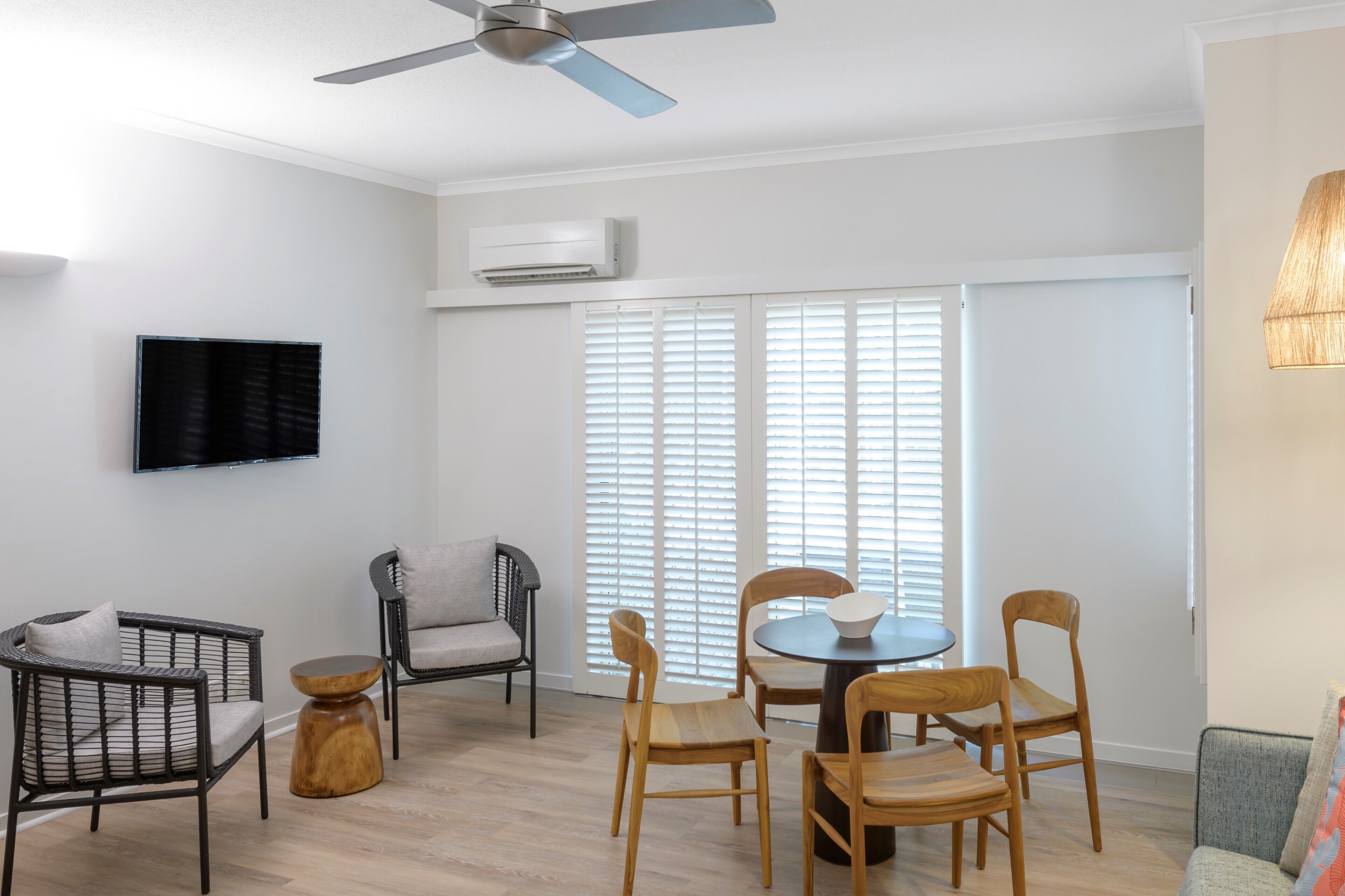 Una sala moderna con ventilador de techo, un televisor de pantalla plana y un comedor con sillas de madera y una mesa redonda.