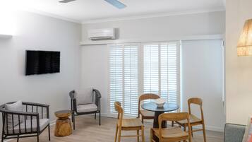 A modern living room with a ceiling fan, a flat-screen TV, and a dining area with wooden chairs and a round table.