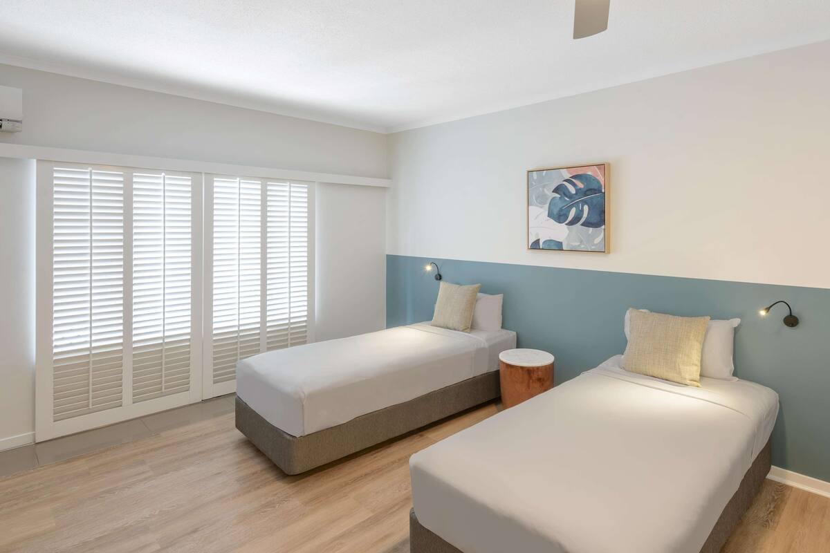 Un dormitorio con dos camas individuales, una mesita redonda pequeña y una lámpara de pared.