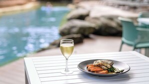 Une table avec un verre de vin blanc et une assiette de nourriture, près d’une piscine.
