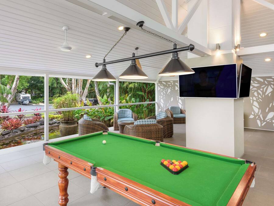 A pool table with a green felt surface, surrounded by wicker furniture and a television mounted on the wall.