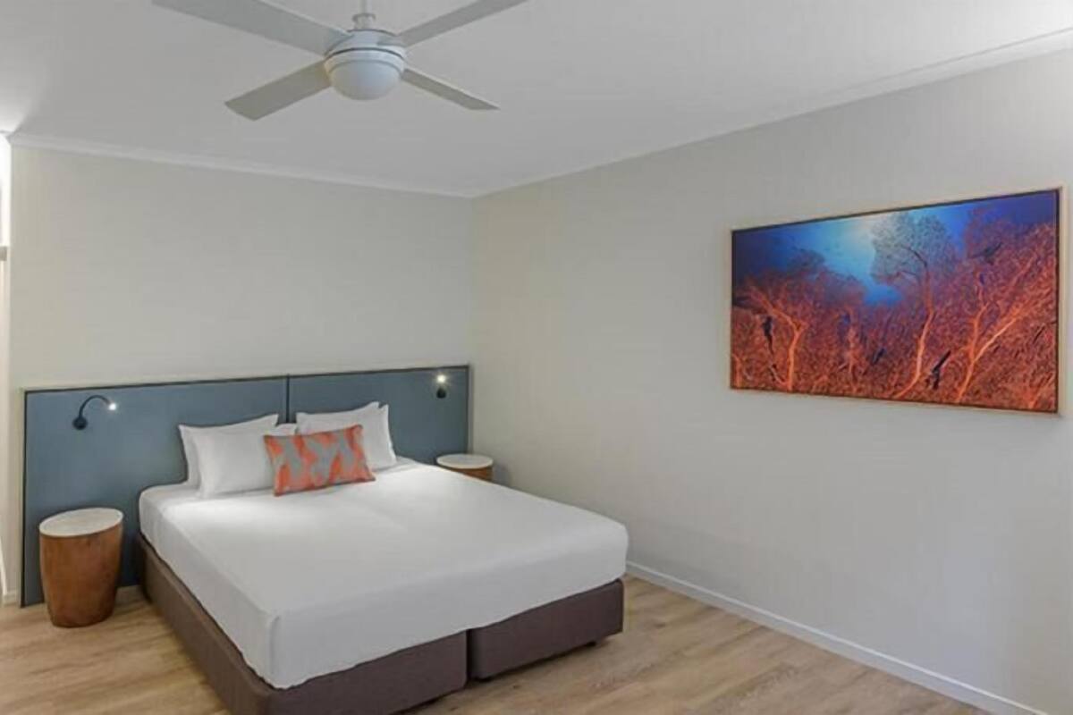 Una habitación de hotel moderna con una cama, mesitas de noche, un ventilador de techo y un cuadro en la pared.
