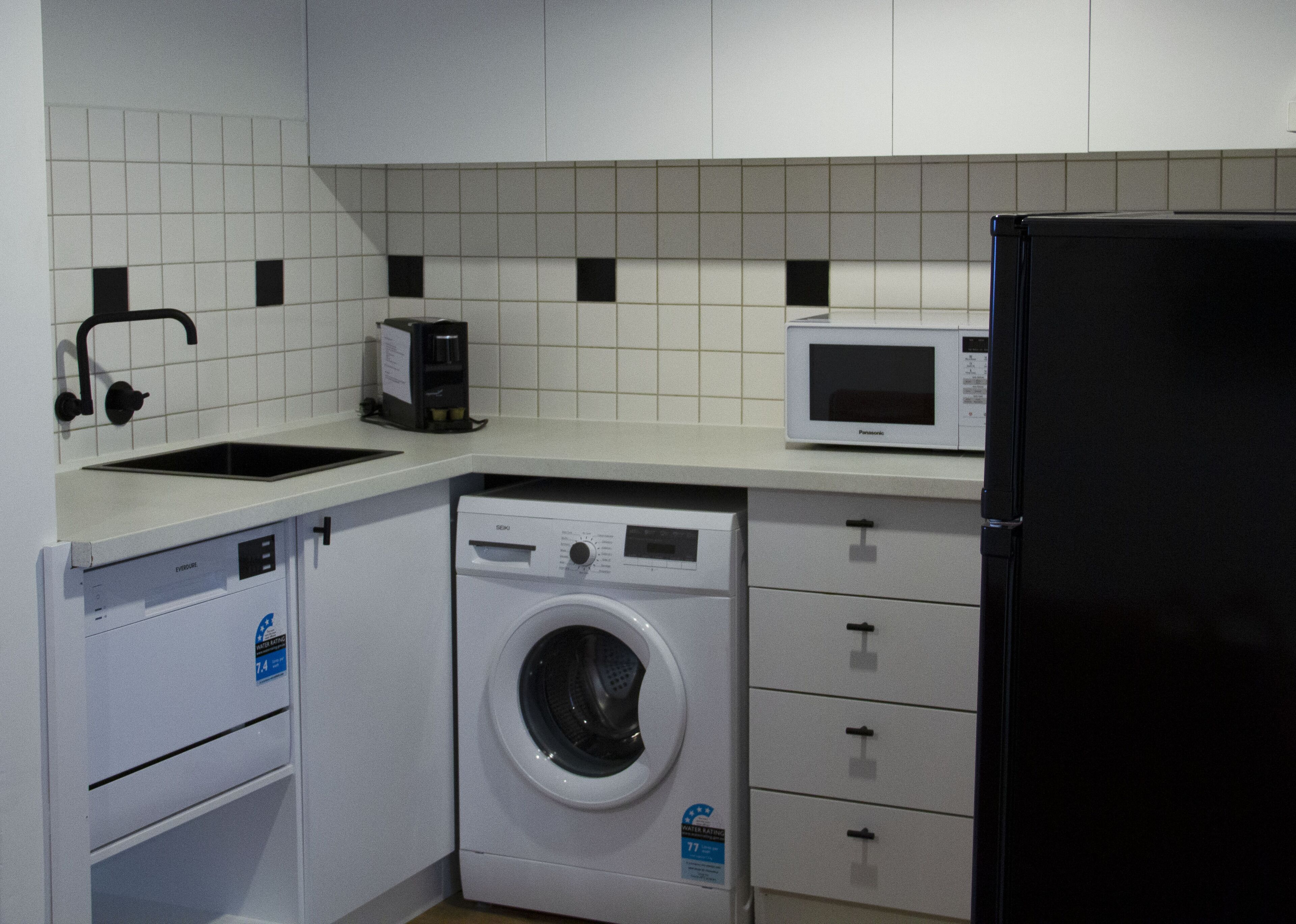 Eine kompakte Küche mit Waschmaschine, Mikrowelle, Kühlschrank und Spüle.