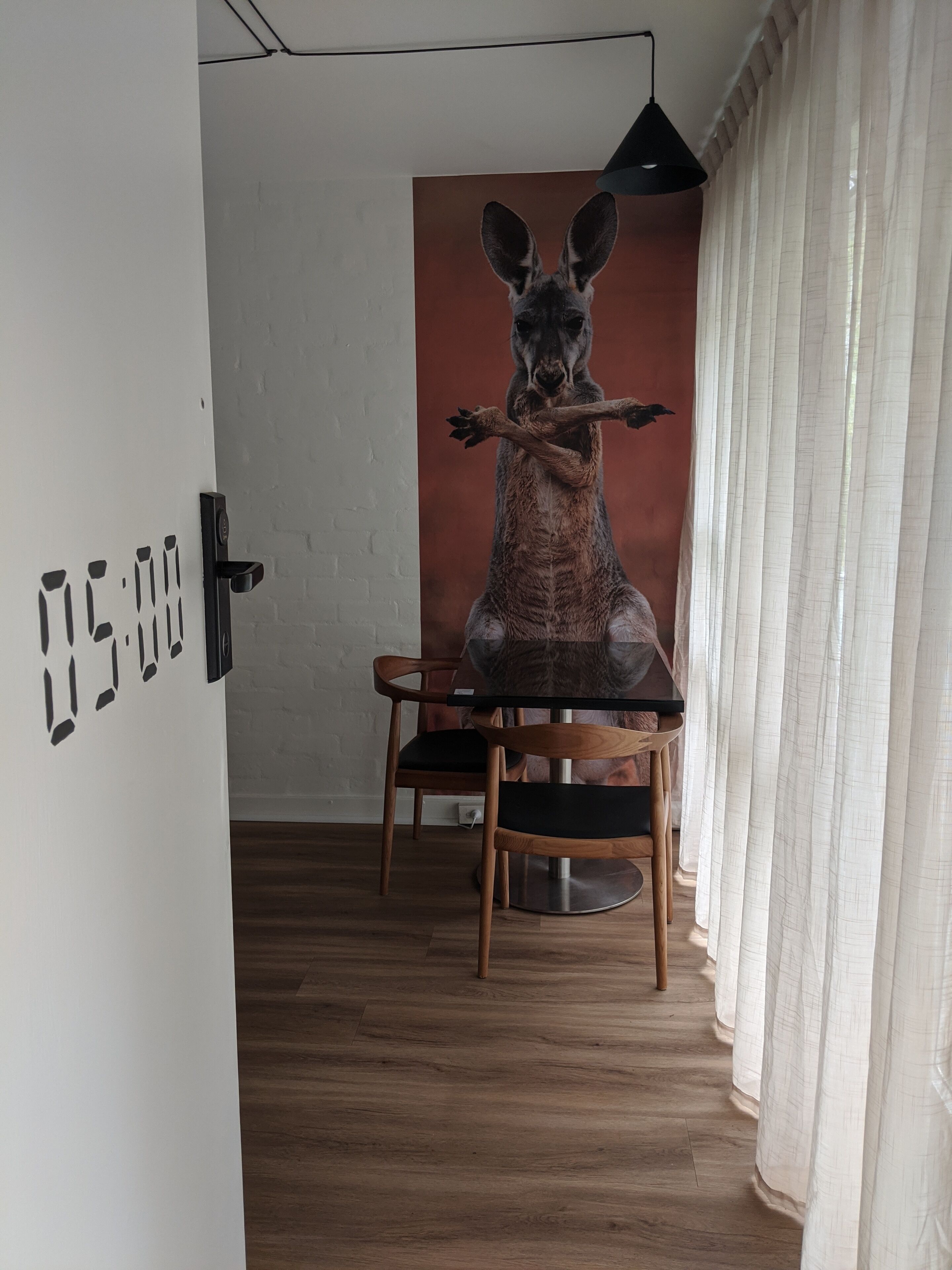 A room with a wooden floor, a table with chairs, a wall clock, and a large kangaroo sculpture.