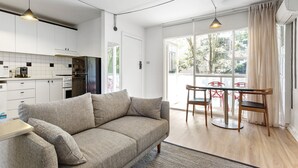 A modern kitchen with white cabinets, a refrigerator, and a dining area with a table and chairs. - SoYa on Davis Apartment Hotel (South Yarra)