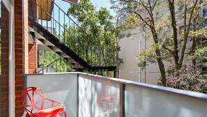 A balcony with a red chair, a glass railing, and a view of trees and a building. - SoYa on Davis Apartment Hotel (South Yarra)
