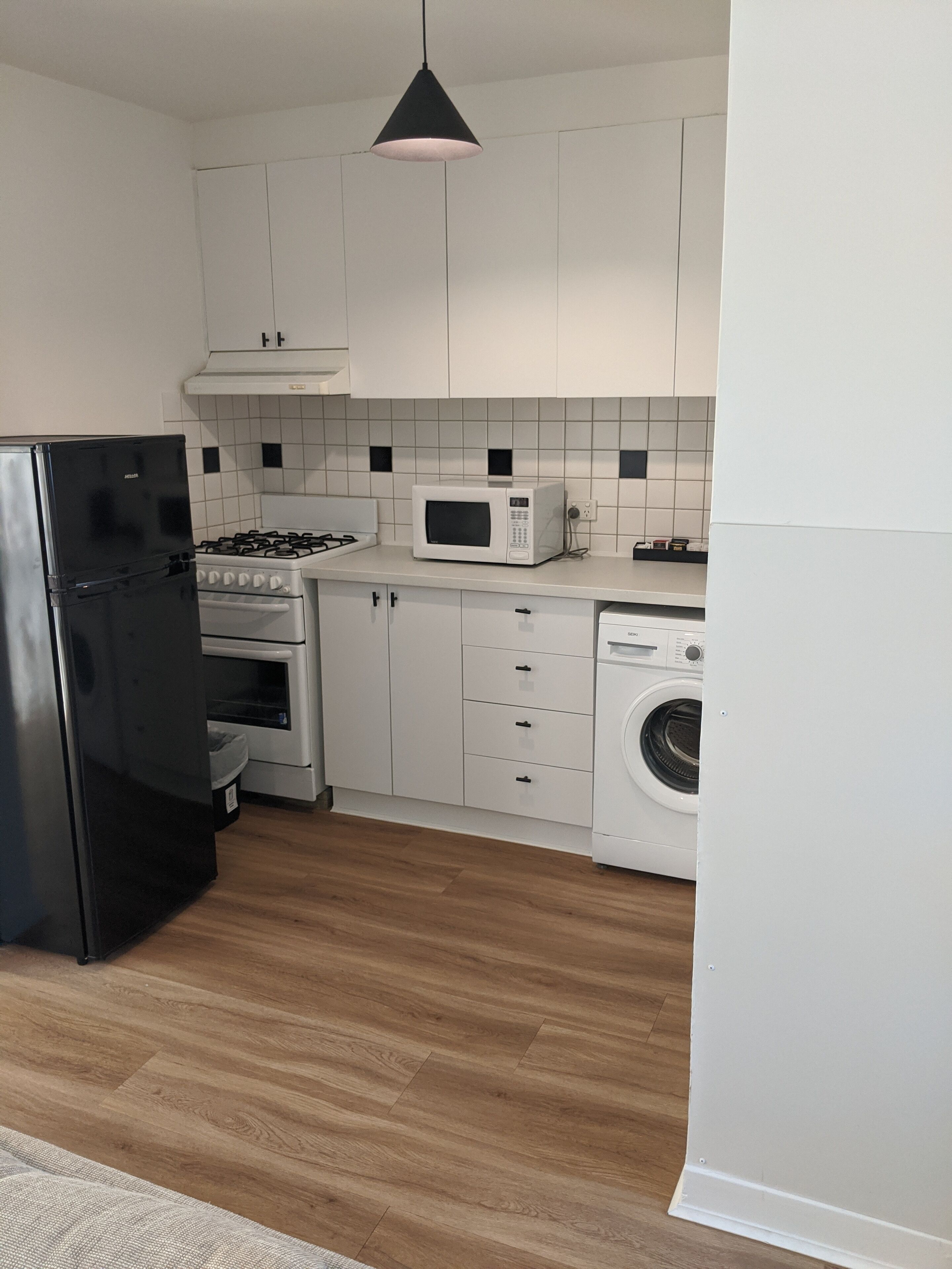 Una cocina moderna con armarios blancos, un refrigerador negro, un microondas, una estufa y una lavadora.