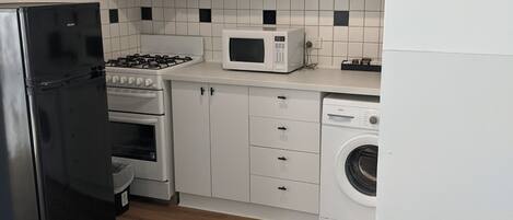 A modern kitchen with white cabinets, a black refrigerator, a microwave, a stove, and a washing machine.