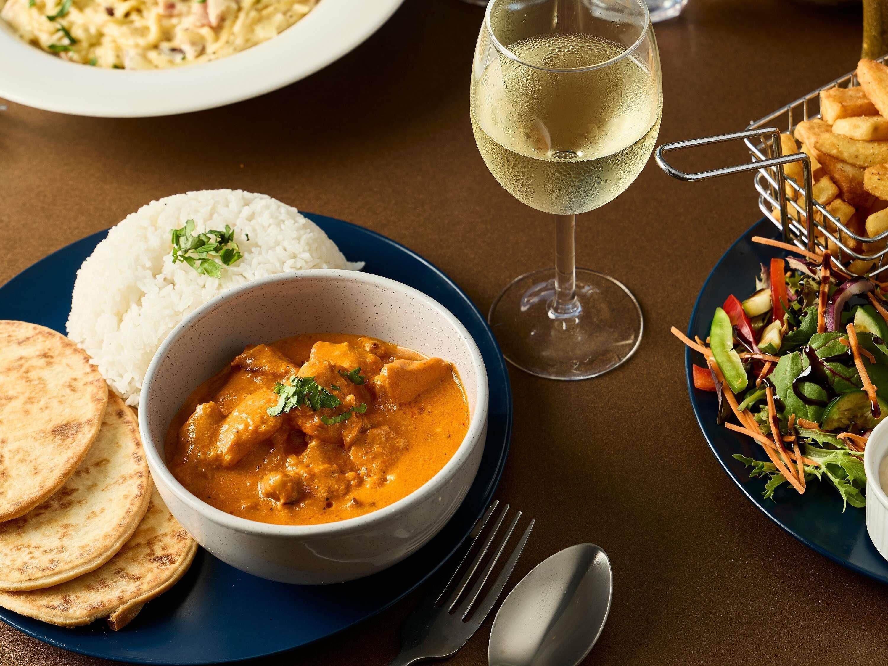 A meal with rice, flatbread, and a bowl of curry, accompanied by a glass of white wine and a salad.