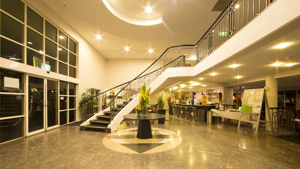 Un'ampia hall con una scalinata centrale, una reception e un'area salotto con tavolo e sedie.
