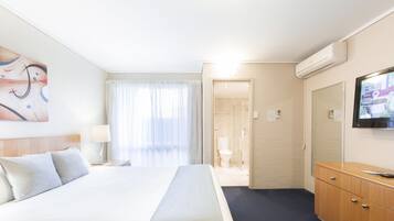 A hotel room with a large bed, a wooden dresser, a television, and a bathroom visible through an open door.