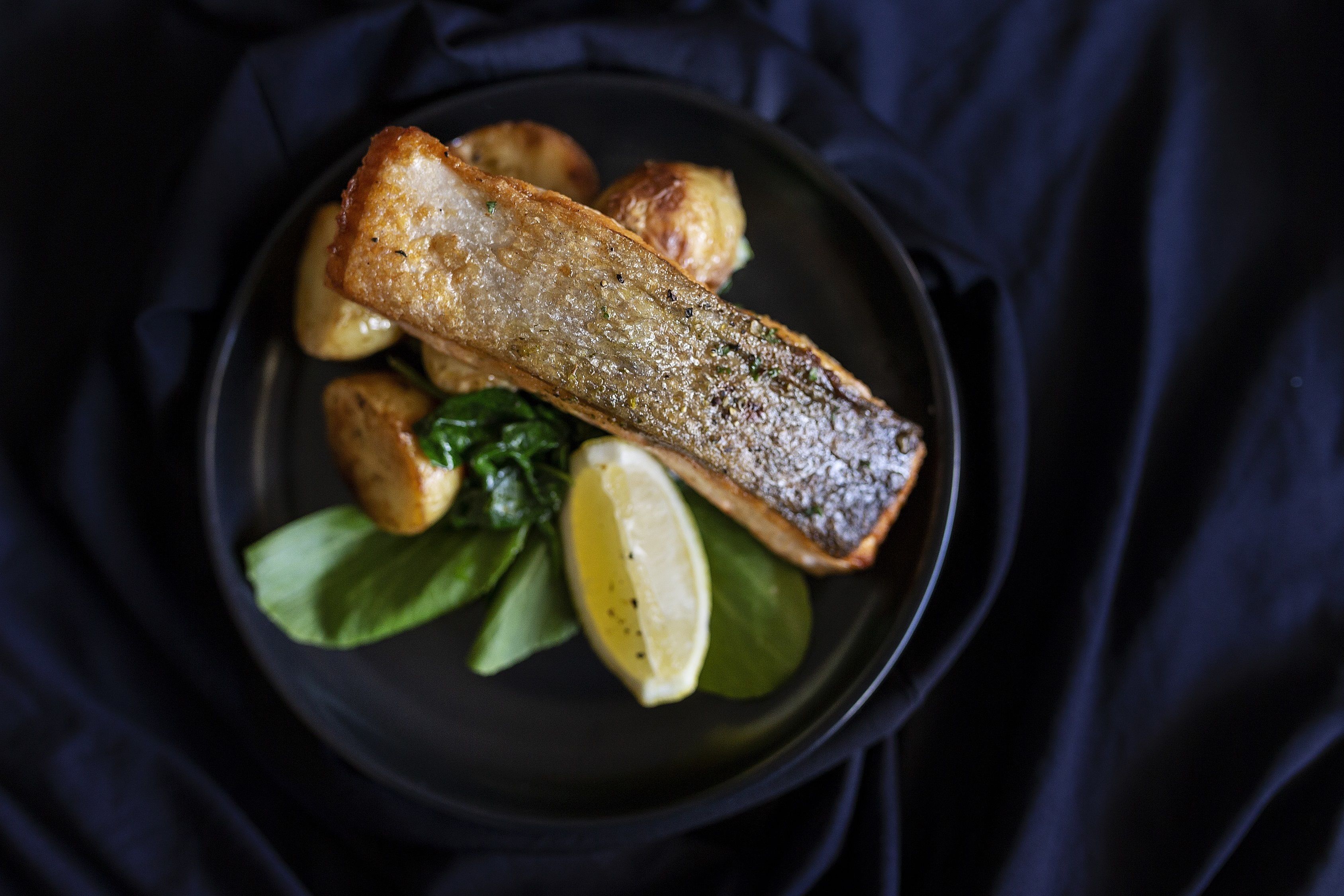 A plate with a piece of fish, potatoes, and greens.
