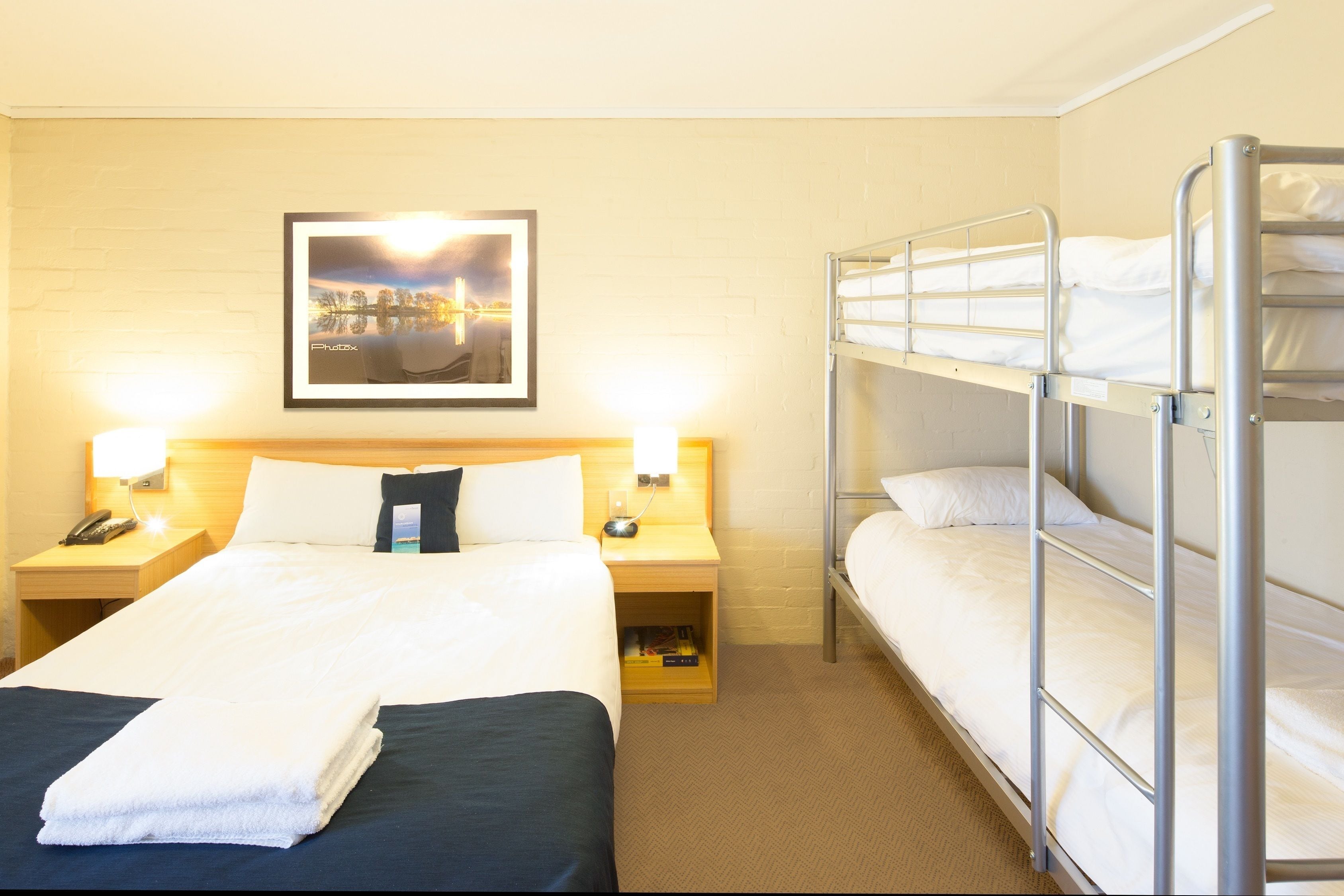 Habitació d'hotel amb un llit individual, una lliterà i un quadre al mur, a més de làmpades de nit.