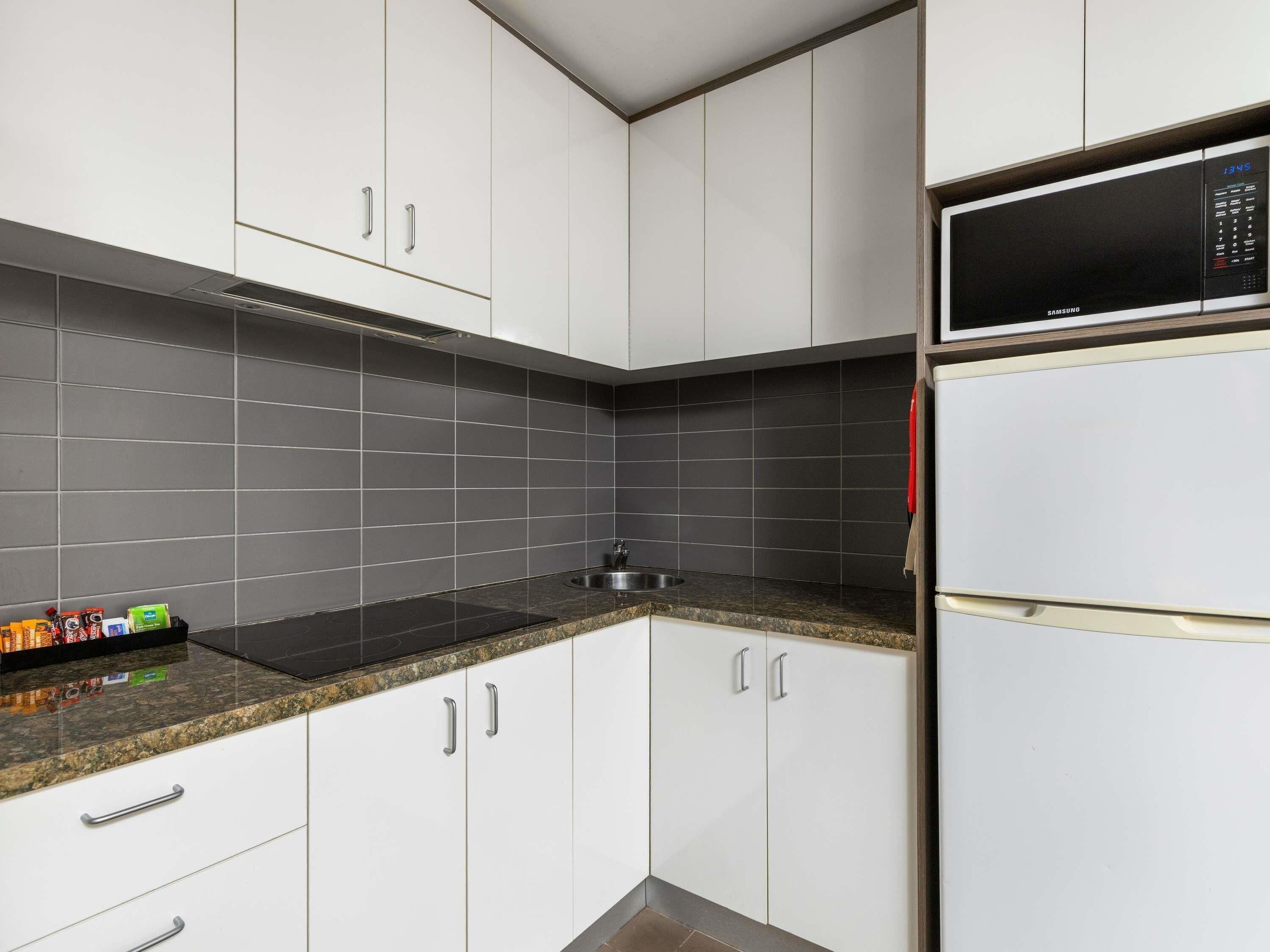 Une cuisine avec des meubles blancs, un micro-ondes noir et un plan de travail en granit.