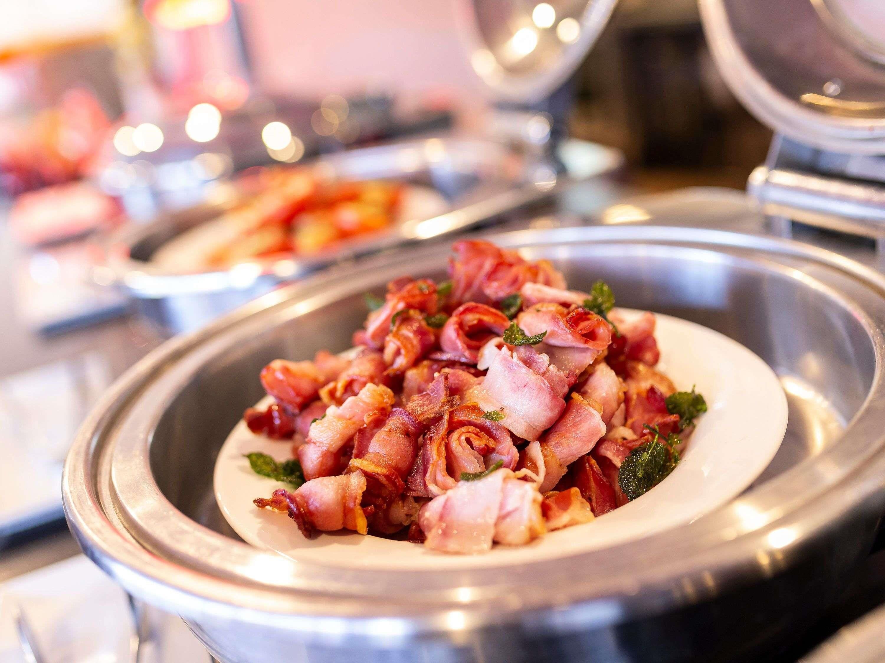 A buffet with a dish of bacon-wrapped items, possibly chicken or fish, garnished with herbs.