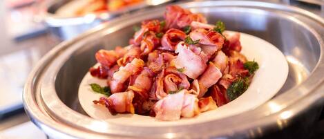 A buffet with a dish of bacon-wrapped items, possibly chicken or fish, garnished with herbs.