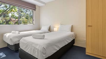 Una habitación con dos camas, una ventana, una lámpara y un armario.
