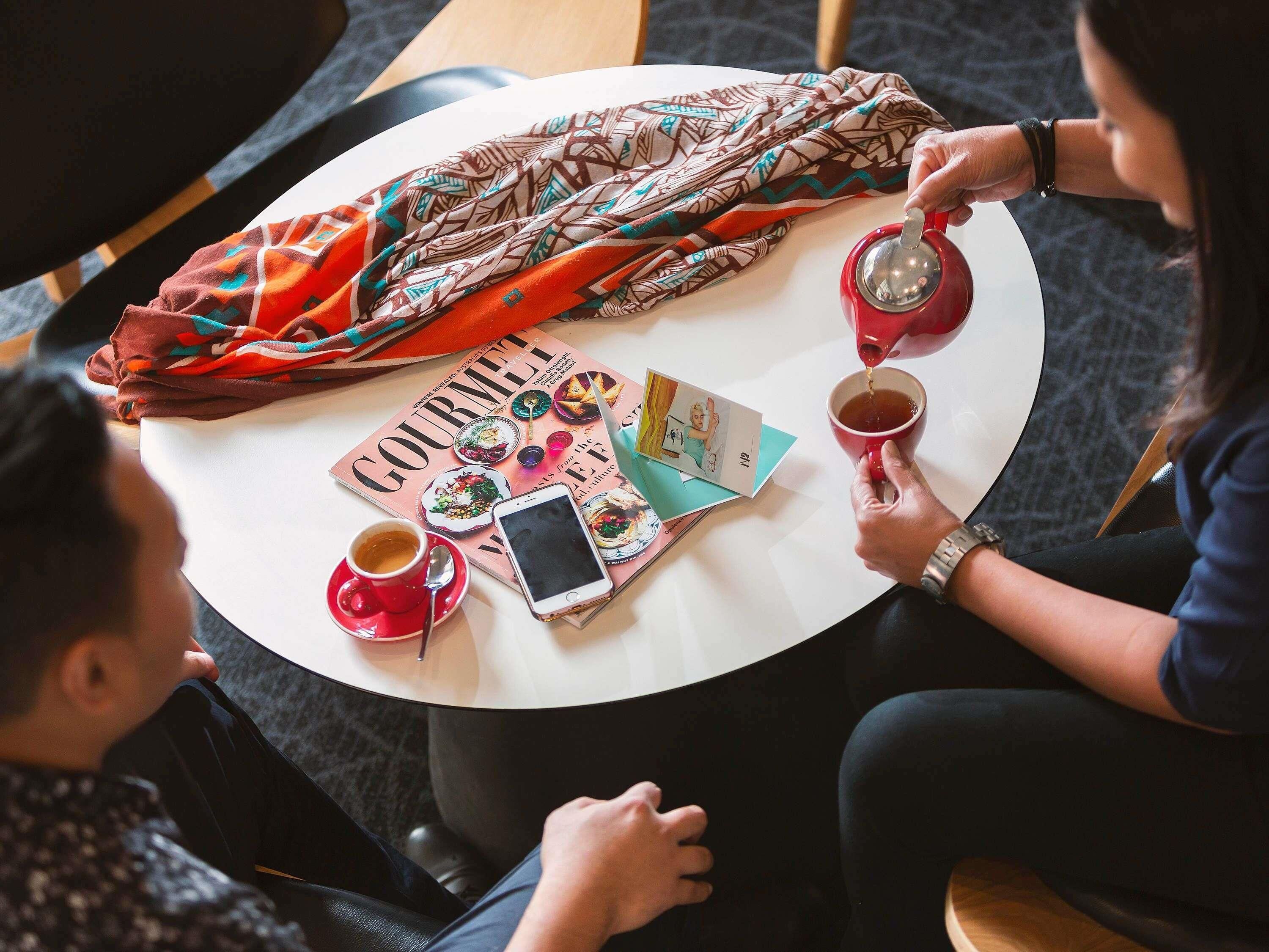 A round table with a magazine, a smartphone, and two cups of coffee.