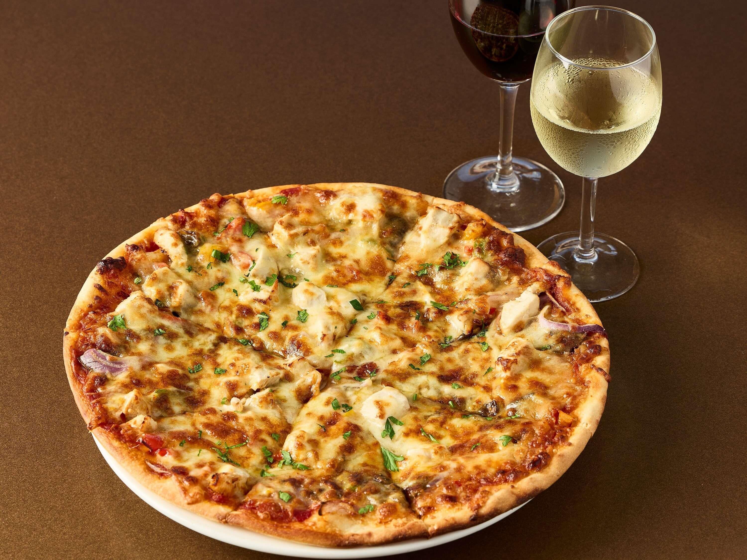 A pizza on a plate with two glasses of wine.