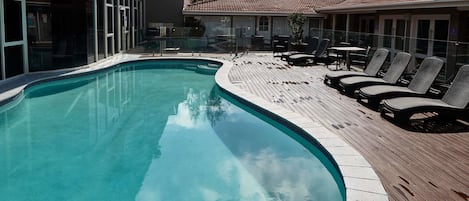 Une piscine avec une terrasse en bois et des chaises longues.