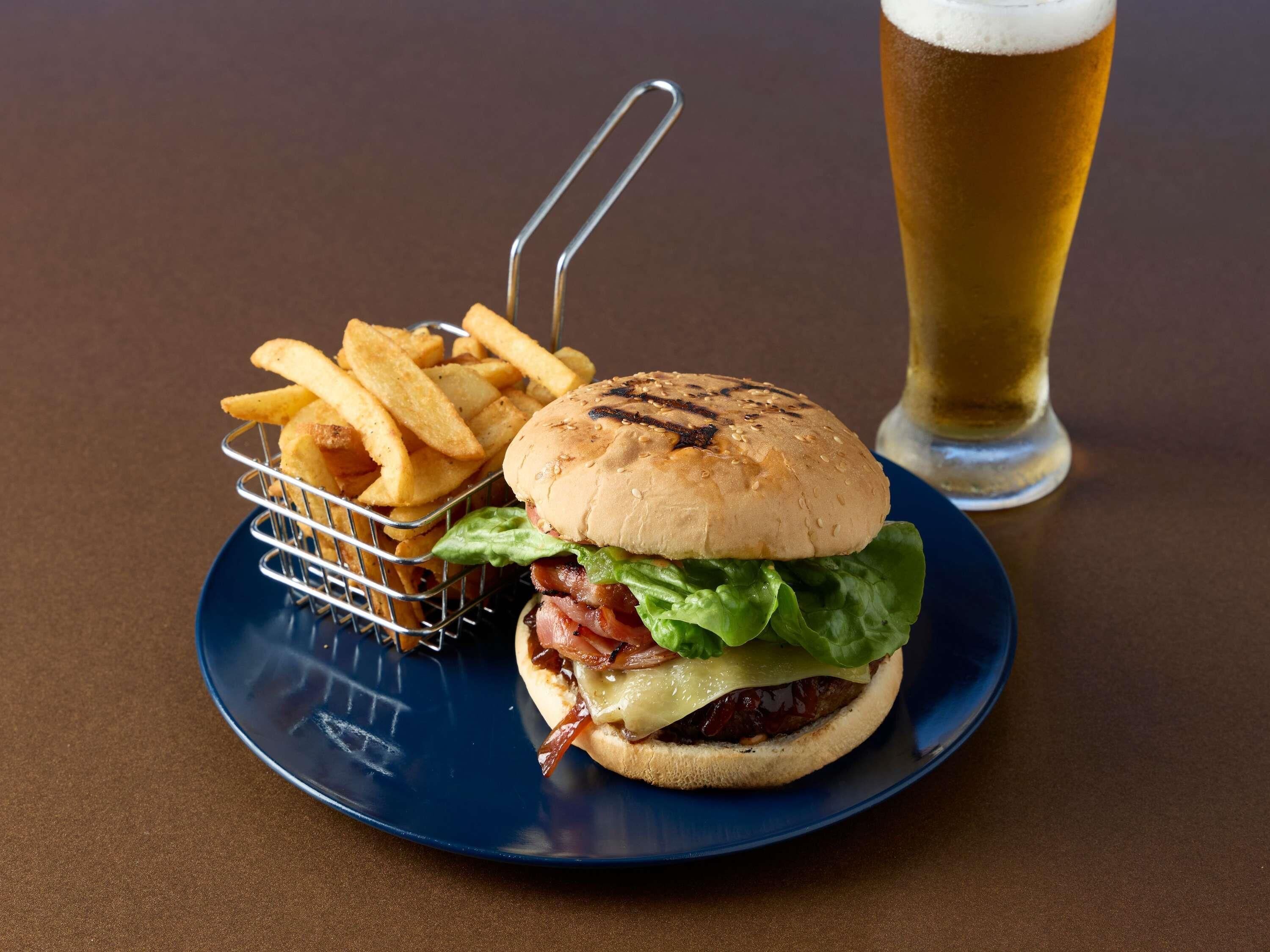 Un hamburger accompagné de frites et d’un verre de bière, le tout servi sur une assiette.