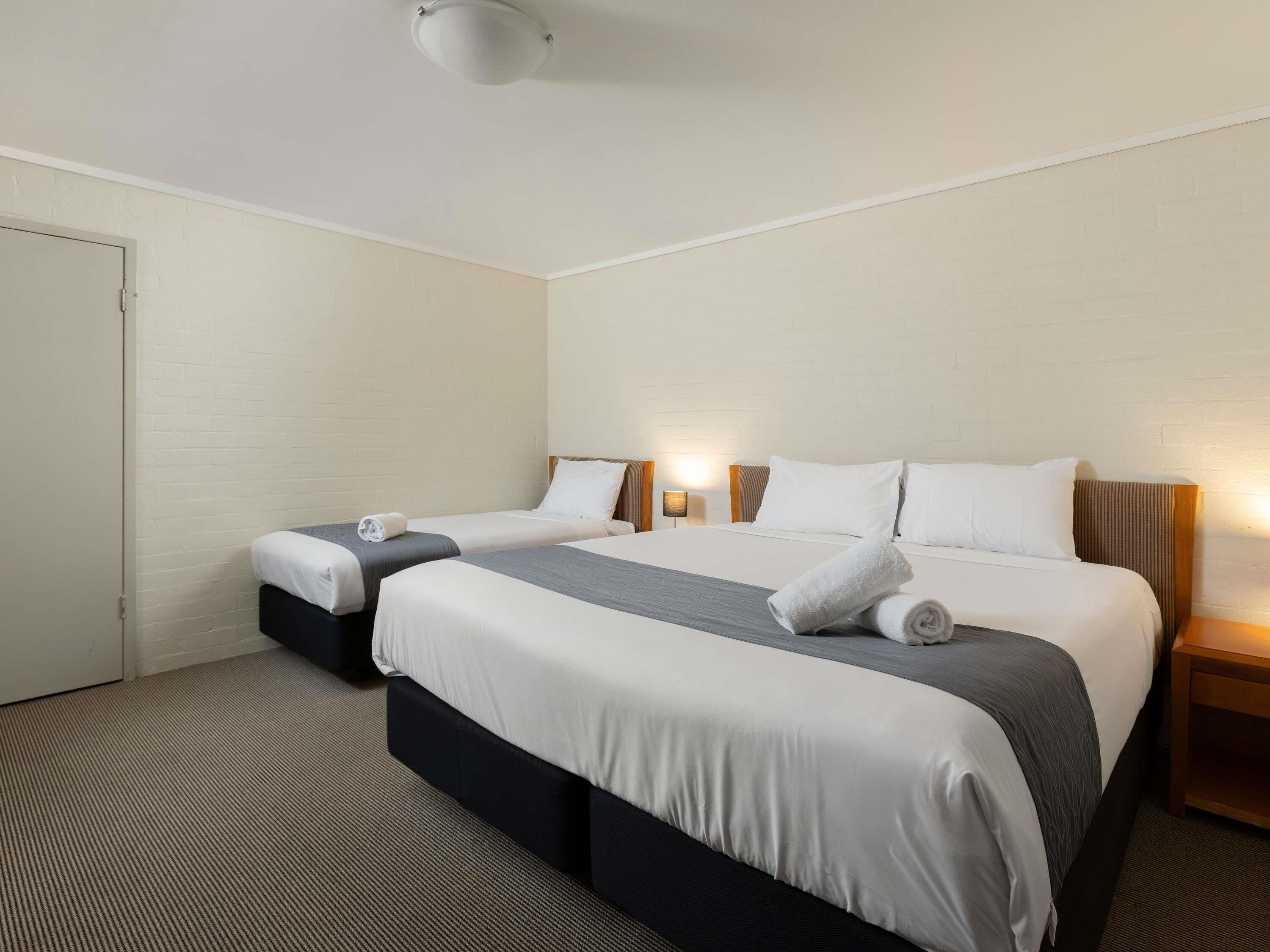 A hotel room with two beds, a carpeted floor, and a white brick wall.
