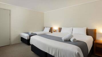 A hotel room with two beds, a carpeted floor, and a white brick wall.