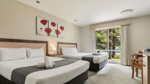 Una camera d'albergo con due letti, una scrivania, una sedia, una finestra con tende e un quadro appeso al muro.