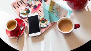 A table with a magazine, a smartphone, two cups of coffee, and a red teapot.