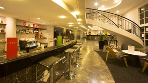 Zona bar moderna con un bancone curvo, sgabelli da bar e una scala che conduce a un livello superiore.