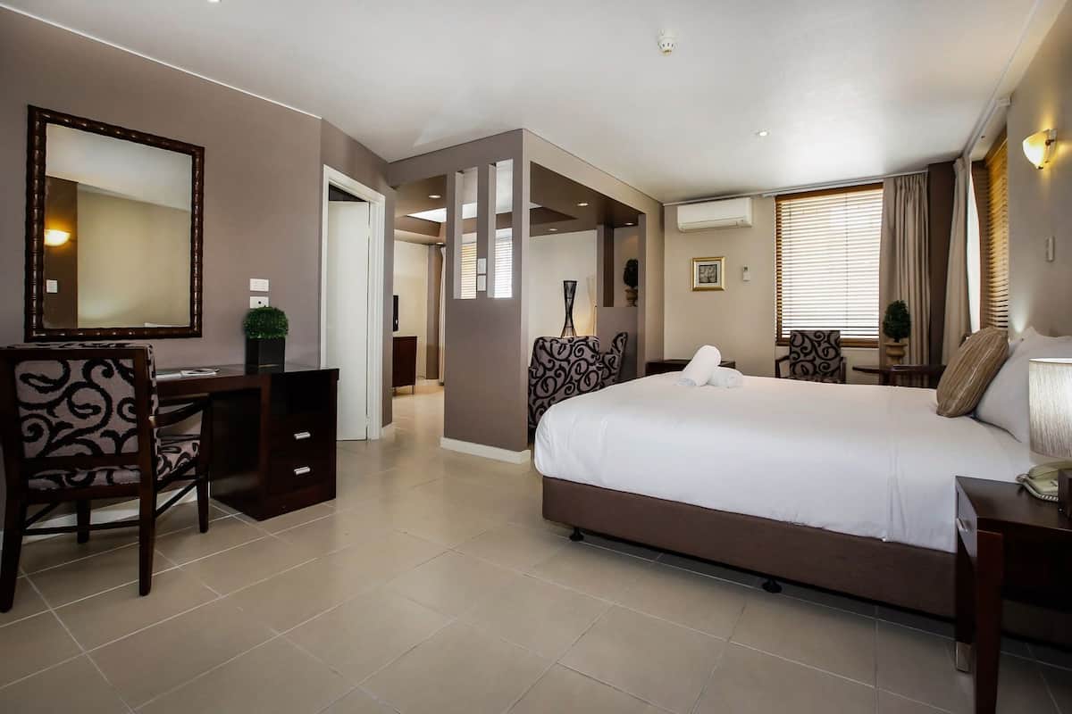 A hotel room with a bed, desk, chair, and a mirror.