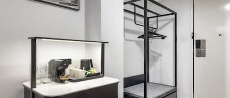 Una habitación de hotel moderna con kitchenette, una silla colgante y una fotografía histórica enmarcada en la pared.