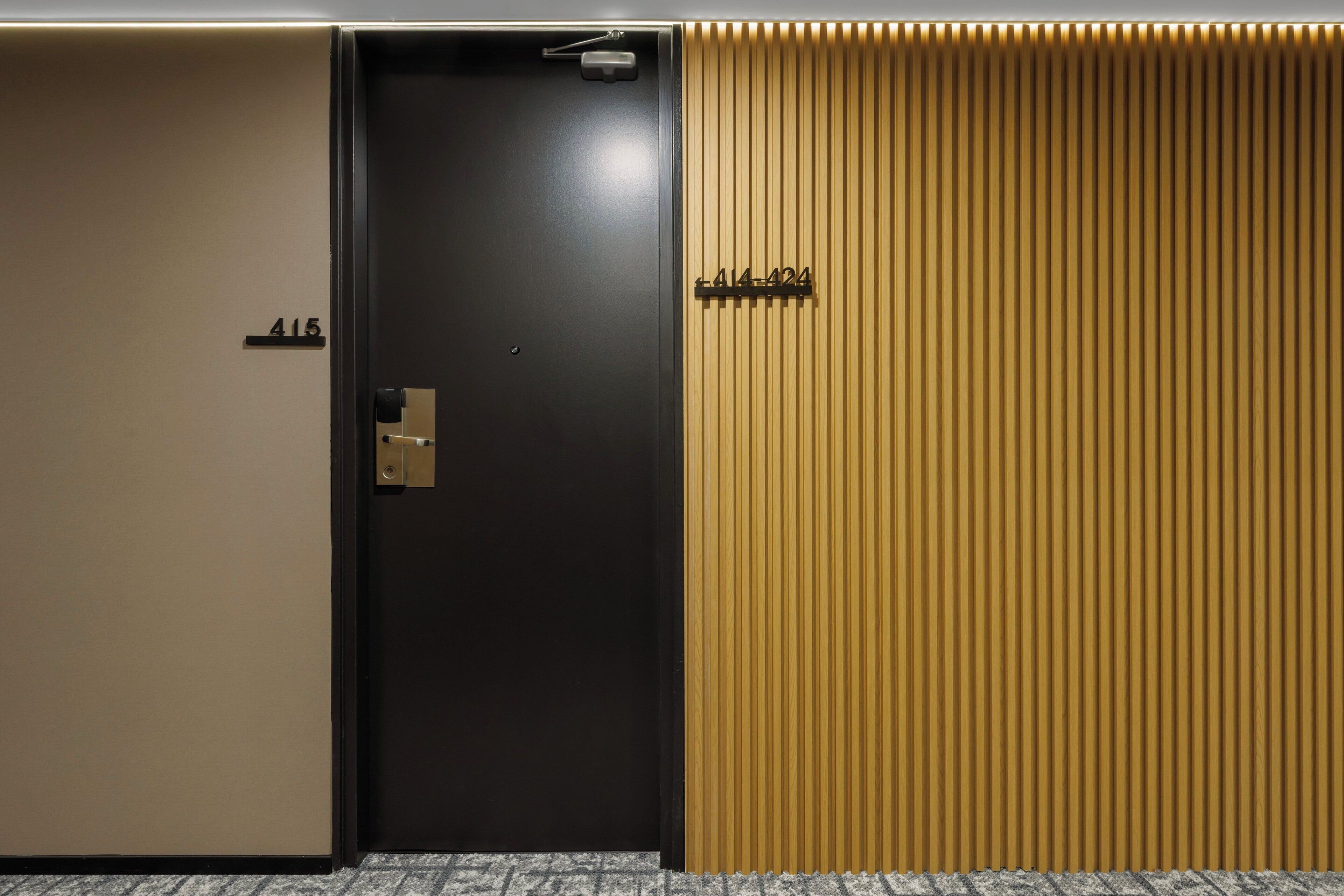 A hotel room with a black door, a beige wall, and a wooden panel wall.