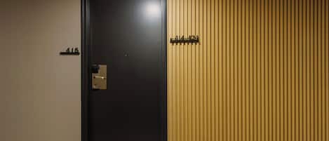 Une chambre d’hôtel avec une porte noire, un mur de couleur beige et un mur recouvert de panneaux en bois.