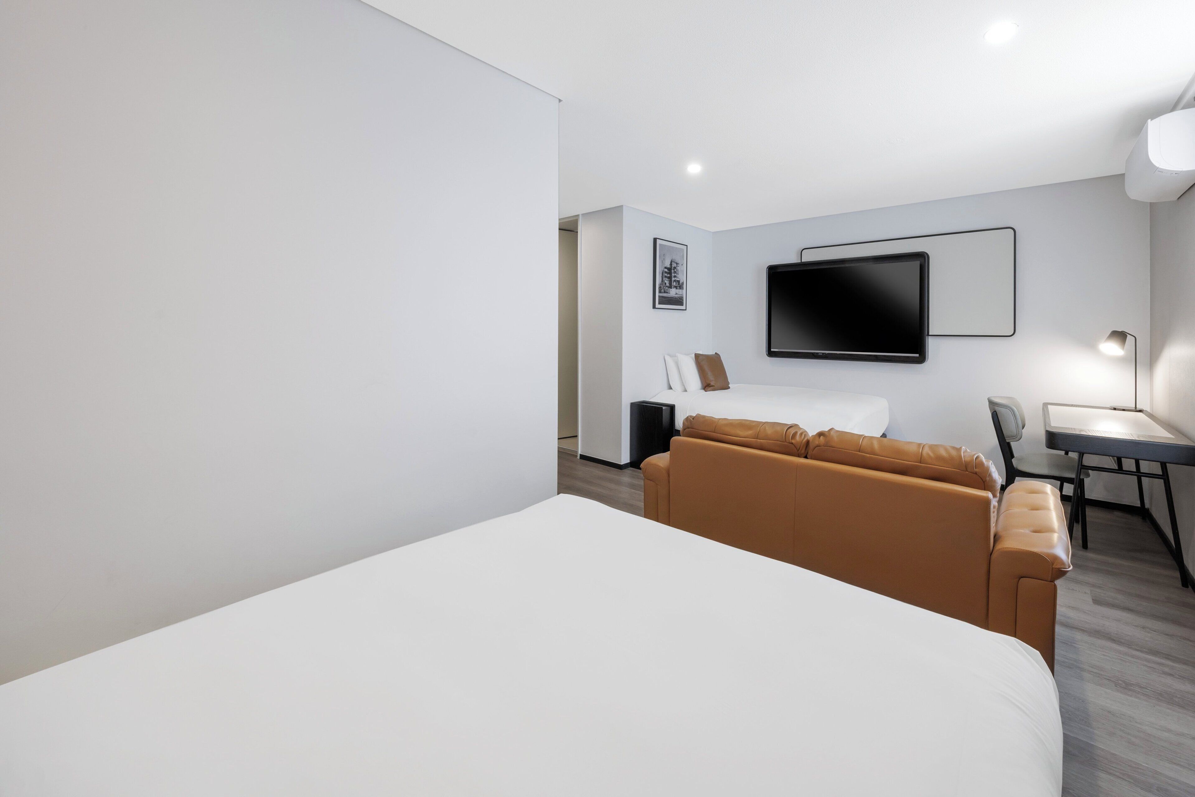 Una habitación de hotel moderna con una cama grande, un sofá, un escritorio con una silla y un televisor de pantalla plana montado en la pared.