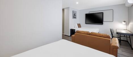 Una habitación de hotel moderna con una cama grande, un sofá, un escritorio con una silla y un televisor de pantalla plana montado en la pared.