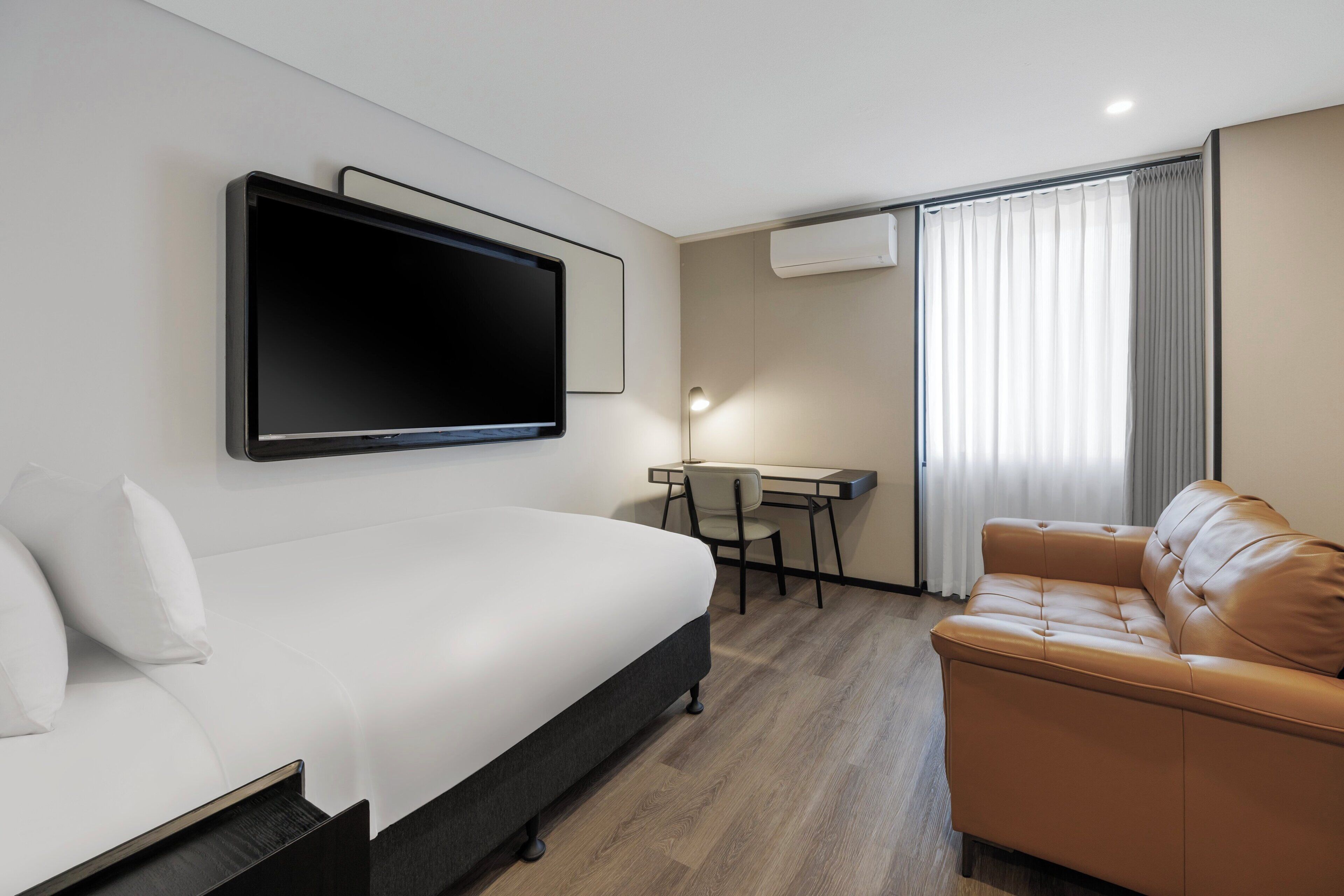 Een hotelkamer met een bed, een bureau, een bank, een televisie en een airconditioning.