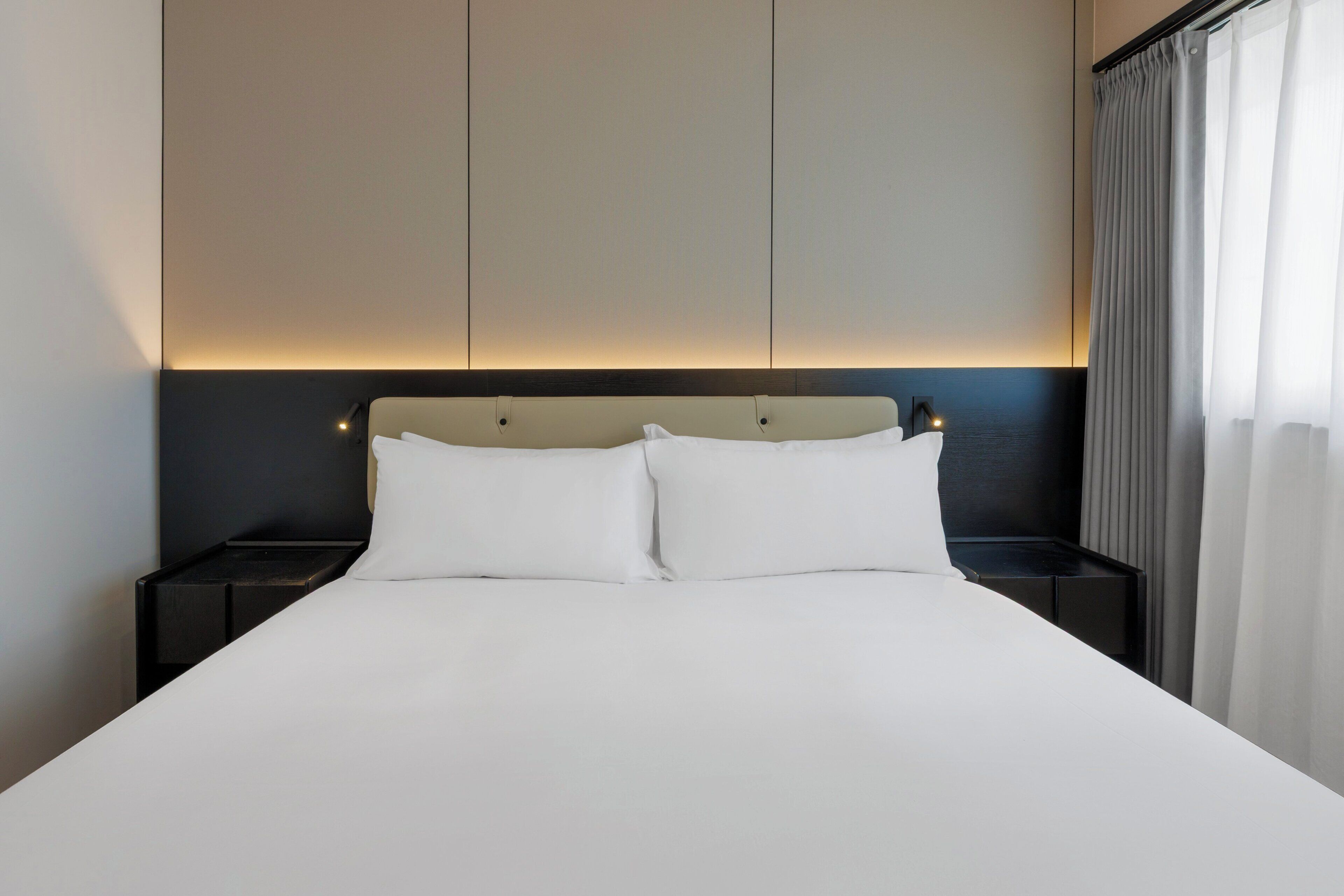 Une chambre d’hôtel avec un grand lit, deux tables de chevet et une tête de lit dotée d’un éclairage intégré.