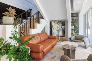 A modern living room with a leather sofa, a round coffee table, and a staircase with a railing. - Holiday Inn Townsville by IHG (Townsville)