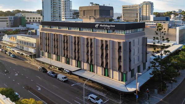 A modern building with a prominent 'Holiday Inn' sign, featuring a multi-story structure with a flat roof and a series of balconies.