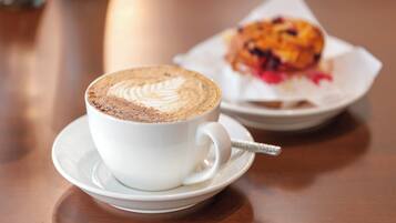 A cup of coffee with latte art on a saucer, a muffin on a plate, and a spoon.