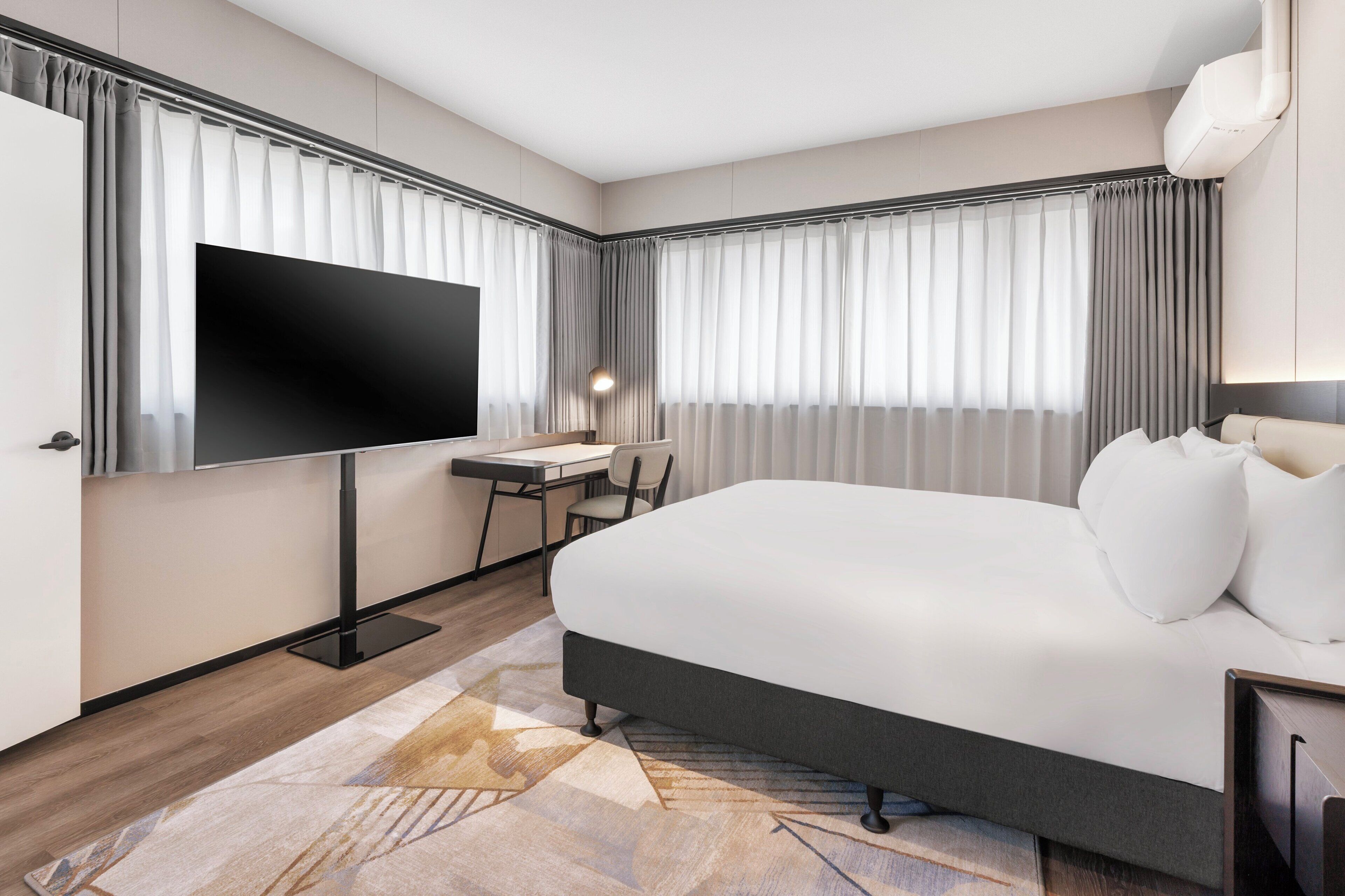Une chambre d’hôtel avec un grand lit, un bureau, une chaise, un téléviseur à écran plat et une fenêtre avec des rideaux.