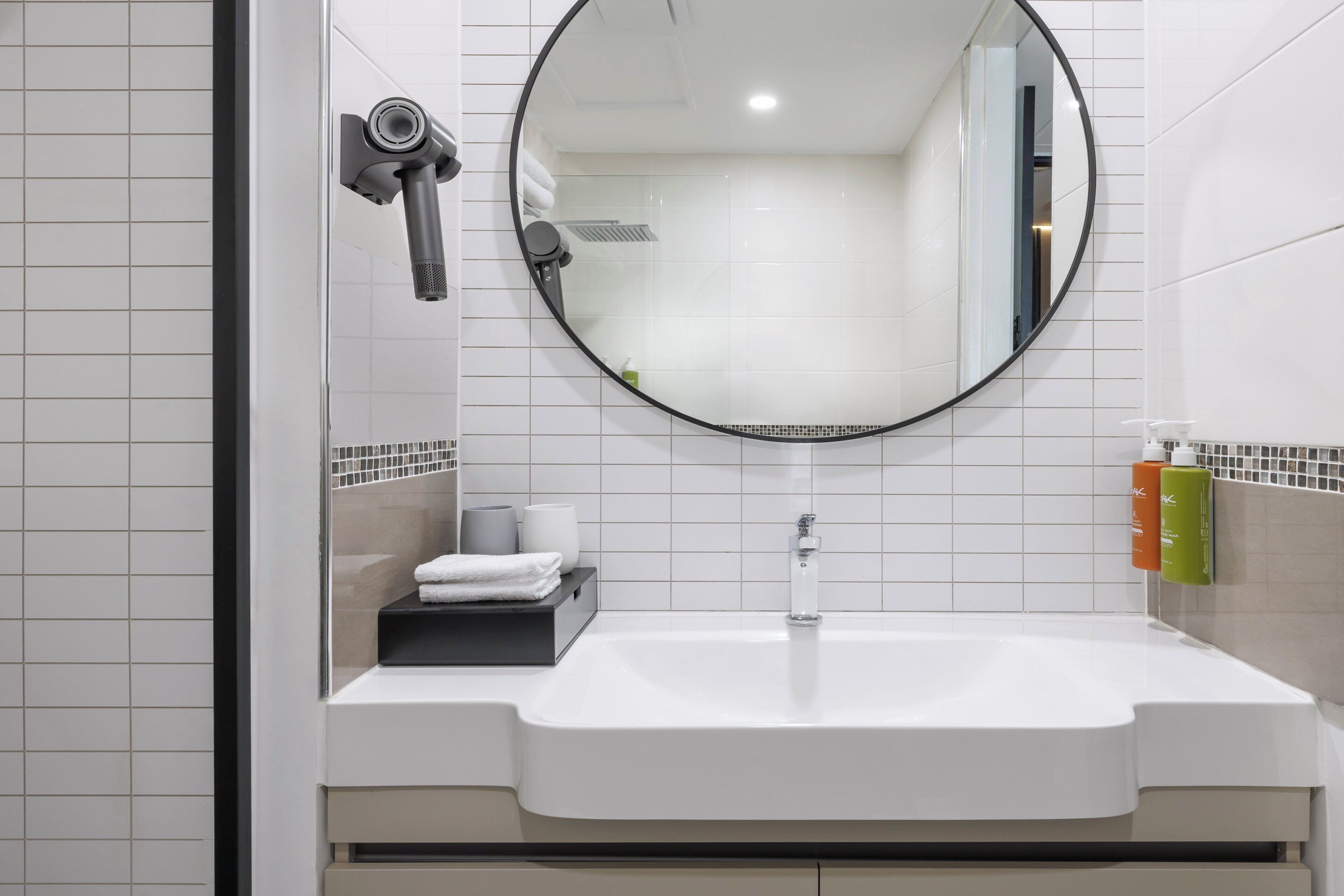A bathroom with a white sink, a round mirror, and a hairdryer mounted on the wall.