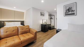 Habitación de hotel moderna con sofá de cuero, cama, una mesita y un cuadro enmarcado en la pared.