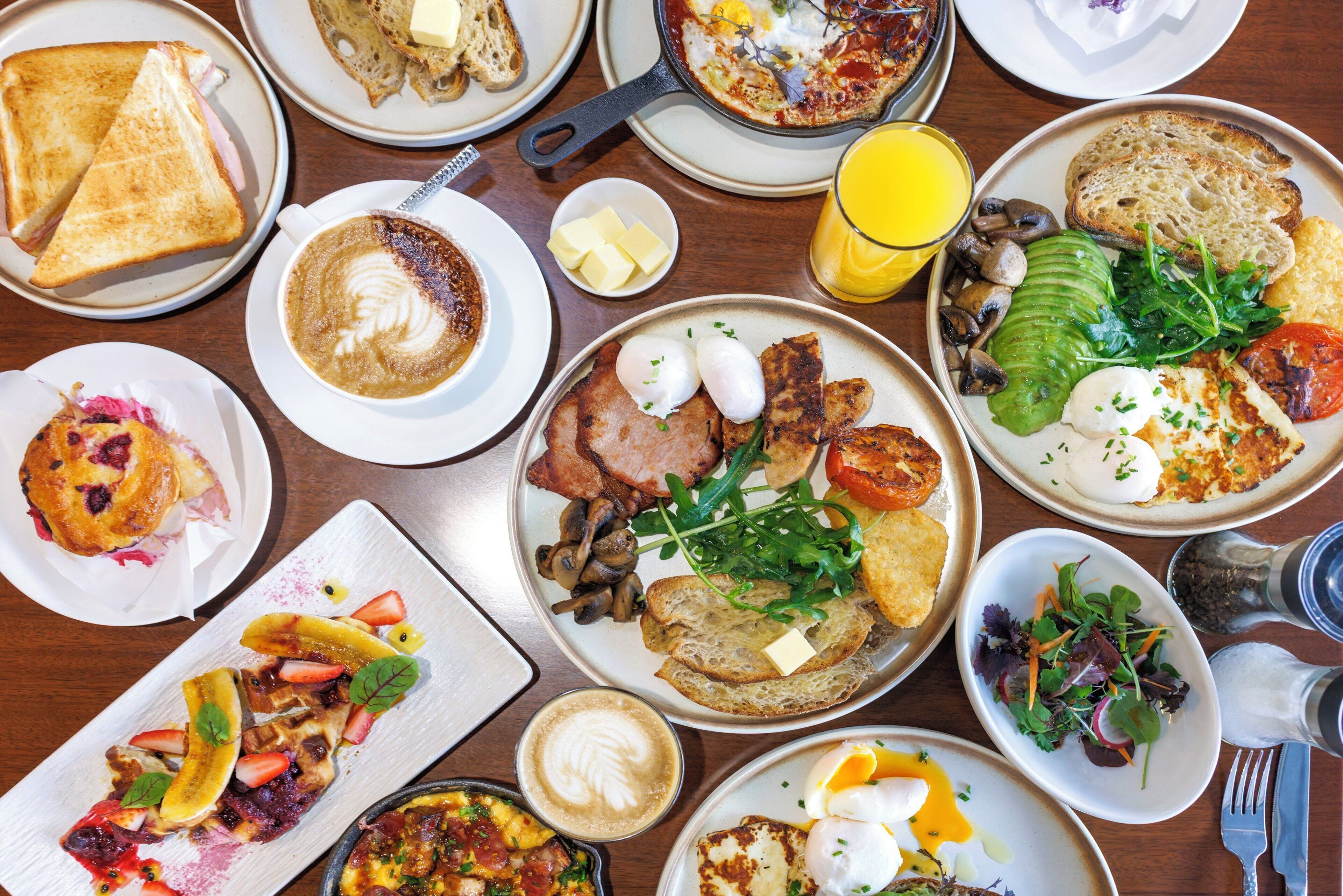 Une variété de plats pour le petit-déjeuner, notamment des toasts, des œufs et des fruits, sont disposés sur une table.