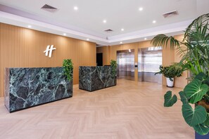 A modern reception area with wooden paneling, marble reception desks, and a large potted plant.
