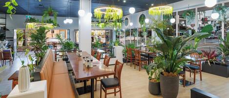 A restaurant with indoor seating, hanging plants, and pendant lighting.
