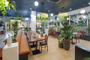 Un restaurante con mesas dentro, plantas colgantes e iluminación colgante.
